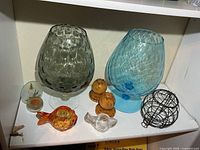 Shelf with oversized grey and blue goblets, small glass pieces, wooden candle holders, wire teapot