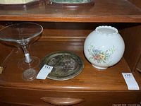 Martini glass, plated tray and floral lamp shade on shelf