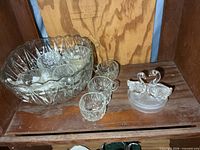 punch bowl containing several cups, additional cups and glass swans on shelf