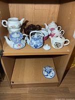 Shelf with six small teapots and miniature tea set below