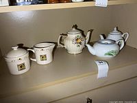 Four items on shelf showing two teapots, creamer and sugar bowl