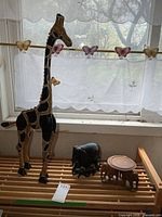 Wooden giraffe, resin elephant circle, and wooden elephant candle stand on slatted surface