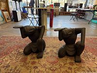 Both wooden kneeling figure stands on rug, full view