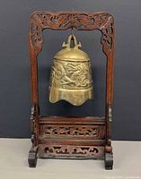 Front view showing brass bell hanging on carved wooden stand