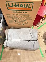Folded grey air mattress with elastic strap in front of U-Haul box