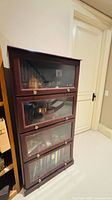 angled front view of four-section oak barrister bookcase showing glass doors and brass knobs
