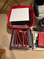 Red bin and purple crate filled with assorted binders, white binder on top
