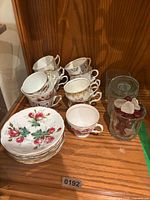 Teacups, small plates, glass vase with faux cherries, empty glass vase