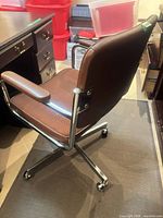 Side view of brown swivel desk chair showing chrome frame, padded armrest, vinyl back