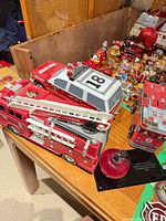 All four items on tabletop: fire ladder truck, emergency SUV, metal piggy bank, glass apple