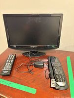 Front view of Insignia 15" TV with both remotes and power adapter on table