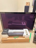 Front view showing Elite plasma TV, center speaker, Samsung WriteMaster, remote, boxed speakers