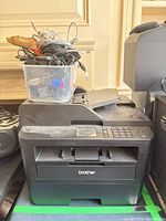 Brother MFC-L2750DW printer with bin of assorted cables on top