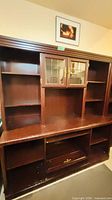 Front view of entire brown wood shelving unit with shelves, glass cabinet and lower storage