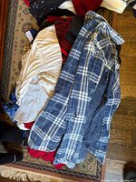 pile of assorted clothing including plaid denim shirt, striped blouse and other garments