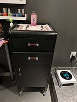 Front view of black salon trolley cart showing drawers, cabinet door and casters