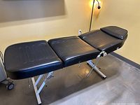 Full side view of black 3-section treatment table on white steel X-frame