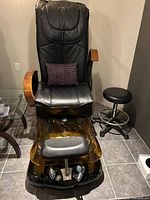 Full view of black pedicure spa chair, amber basin, operator stool, pillow