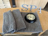 Stacked gray chenille mats, black round clock, metal letters SPA on table