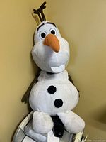 Front view of Olaf plush seated against wall