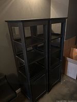 Front view of both tall narrow black bookcases showing open shelves and cabinet doors