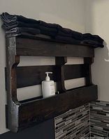Front view of dark brown wooden wall shelf with towels and soap for scale