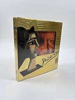 Front view showing gold metallic dust jacket with cut-out window displaying Picasso artwork and portrait