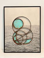 Front view of framed mixed-media artwork showing circular steel forms over seascape background