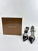 Gucci shoe box beside pair of black ankle-tie pumps