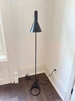 Full view of black AJ floor lamp standing against wall, power cord visible