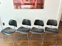 Front view of four black Eames DCM chairs aligned on wood floor
