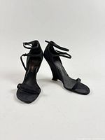 front and side view of black leather wedge sandals showing curved wedge heels and ankle straps