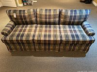 Front view of plaid three-cushion sofa with rolled arms and skirt