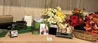 Wide shot of all items on table including artificial flowers, floral supplies, picture frames and basket