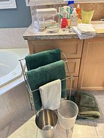 Overall view showing towel rack with towels, two wastebaskets, towels on floor and countertop items