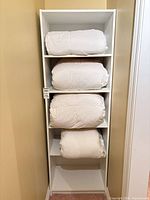 Three white duvets and body pillow stored on white shelving unit
