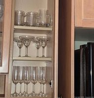 cabinet view showing mugs, margarita glasses and champagne flutes on three shelves