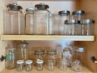 Upper shelf of cabinet showing large and small glass canisters with stainless steel lids