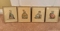 Four framed fashion prints leaning against wall