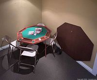 Octagonal poker table with chairs, chip set, cards and brown cover leaning on wall