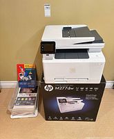 Printer sitting on its retail box next to clear bin of supplies