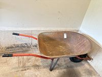 Side view of metal wheelbarrow showing tray, wheel, red handles