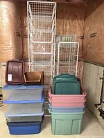 Stacks of plastic storage bins various colours and clear plus two wire basket tower organizers behind