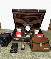 Lot overview showing briefcase open with clocks, binoculars, radio, padlocks not visible