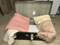 Open black steamer trunk with blankets and sheet set inside