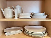 Cabinet shelf showing teapots, bud vase, stack of oval baking dishes, stack of oval platters, nested rectangular dishes