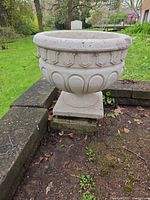 Front view of concrete urn planter on pedestal, showing decorative motifs and overall shape