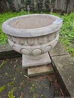 Concrete urn planter on pedestal, full side view displaying decorative details and visible crack at pedestal base