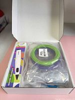 Box opened showing 3D pen package at left and sealed green filament coil with accessory bag