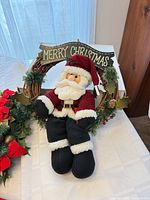 Plush Santa sitting inside grapevine wreath with Merry Christmas sign